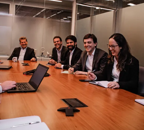 Grupo de executivos sorrindo e conversando sentados ao redor de um mesa de madeira