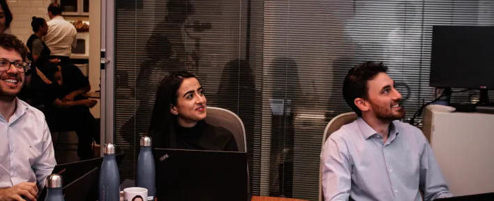 Três pessoas sentadas sorrindo em um ambiente corporativo