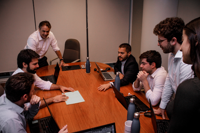 Grupo de pessoas sentadas ao redor de mesa com computadores