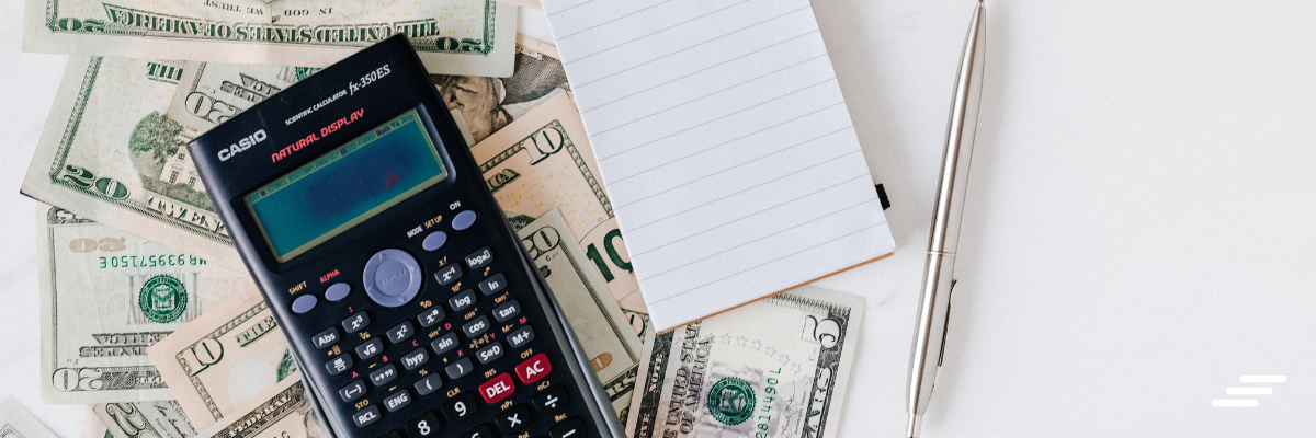 Calculadora, cédulas de dinheiro e bloco de notas sobre a mesa, representando a revisão de despesas do Orçamento Base Zero